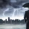 Businessman standing in front of storm clouds with umbrella